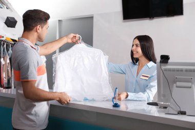 Bayan işçi kuru temizlemecideki müşteriye gömlek veriyor.