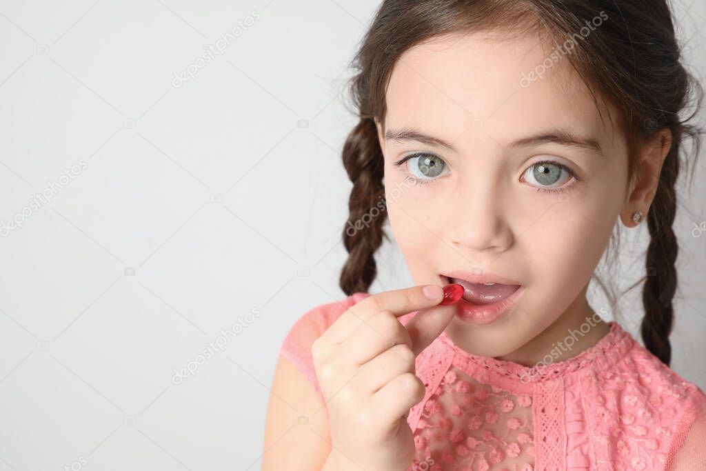 Little girl taking vitamin capsule on light background. Space for text