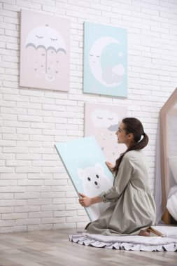 Dekoratör beyaz tuğla duvara resim asıyor. Çocuk odası iç tasarımı.