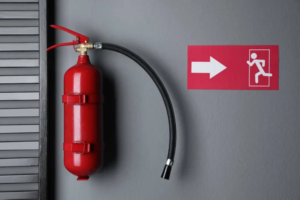 Fire extinguisher and emergency exit sign on grey wall indoors