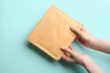 Açık mavi arkaplanda Kraft kağıt zarf tutan kadın, yakın plan.