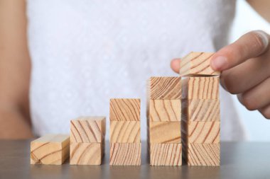 Gri masada tahta bloklarla merdivenler inşa eden kadın, yakın plan. Kariyer basamağı