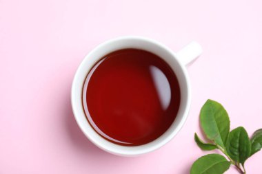 Bir fincan aromatik siyah çay ve pembe arka planda yeşil yapraklar.