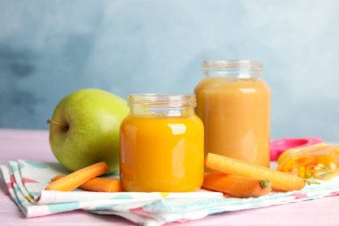 Kavanozlarda sağlıklı bebek maması ve açık mavi arka planda pembe ahşap masada taze malzemeler.
