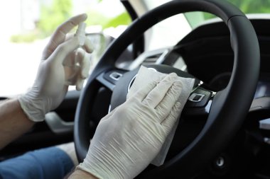 Islak mendille direksiyonu temizleyen adam ve arabada antibakteriyel sprey, yakın plan.