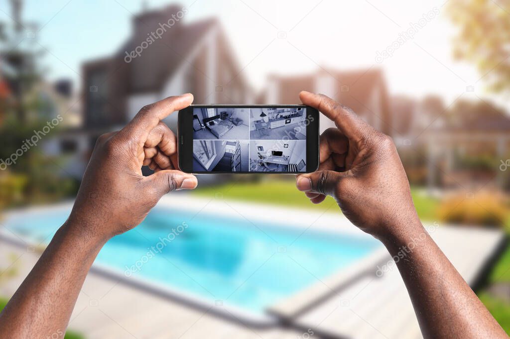 African-American man monitoring modern CCTV cameras on smartphone near his house, closeup. Home security system