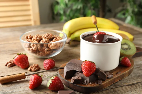 Fondue pot with chocolate and different products on wooden table