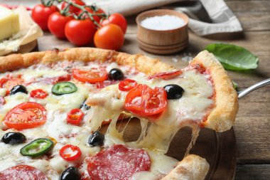 Lezzetli pizzadan bir dilim Diablo alıyorum ahşap masada, yakın plan.