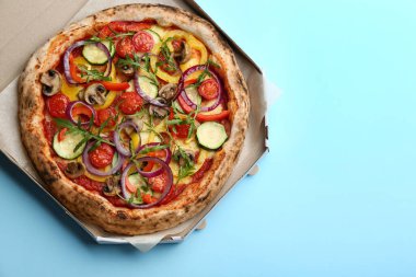Açık mavi arka planda karton kutuda nefis sıcak sebze pizzası, üst manzara. Metin için boşluk