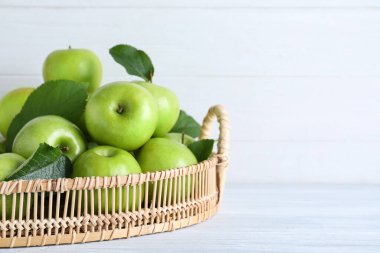 Sulu yeşil elmalar hasır tepside beyaz ahşap masada, yakın plan. Metin için boşluk