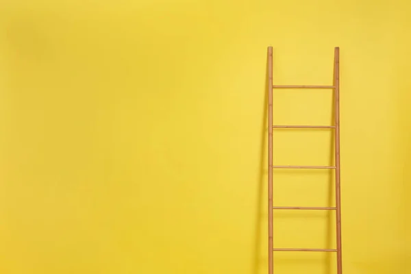 Modern wooden ladder on yellow background. Space for text