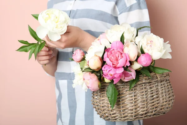 ベージュの背景にバスケットに美しい牡丹の花束を持つ女性 — ストック写真