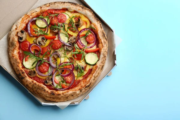 Delicious hot vegetable pizza in cardboard box on light blue background, top view. Space for text