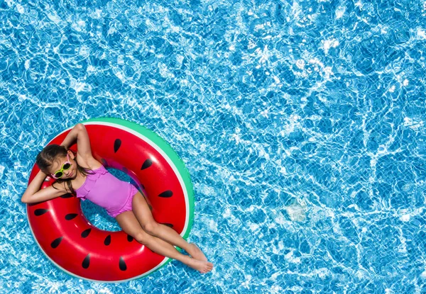 Cute little girl with inflatable ring in swimming pool, top view. Space for text