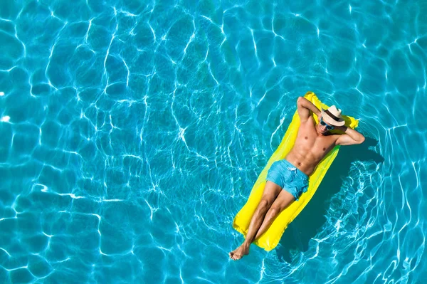 Young man with inflatable mattress in swimming pool, top view. Space for text