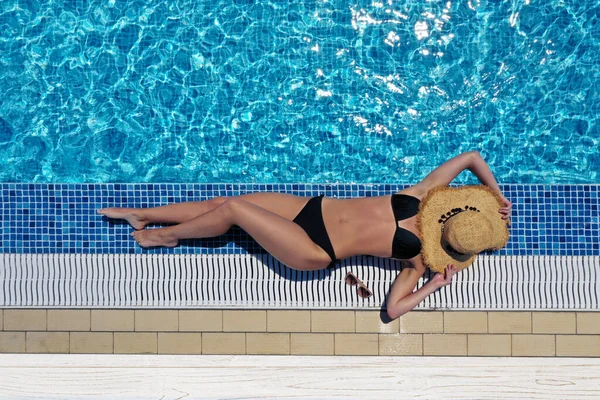 Young woman with hat lying near swimming pool, top view