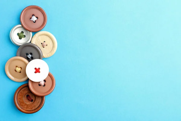 Many colorful sewing buttons on light blue background, flat lay. Space for text