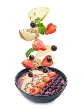 Acai çilekleri ve diğer malzemeler beyaz arka planda kaseye dökülüyor.