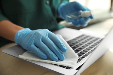 Lastik eldivenli bir kadın laptopunu ıslak mendille temizliyor.