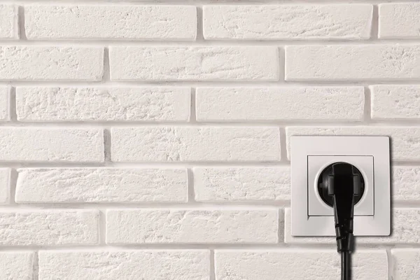 White brick wall with power socket and inserted plug, space for text. Electrical supply
