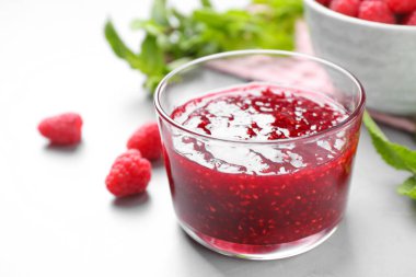 Lezzetli reçel ve taze ahududular gri masada, yakın plan.