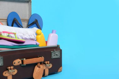 Açık mavi arka planda farklı plaj eşyalarının olduğu klasik bir bavul. Mesaj için yer var. Yaz tatili