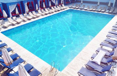 Güneşli bir günde havuz kenarında şemsiyeli şezlonglar. 