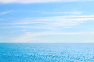 Mavi gökyüzünün altında bulutlu dalgalı bir deniz.