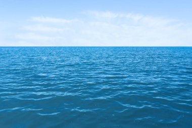 Mavi gökyüzünün altında bulutlu dalgalı bir deniz.