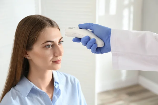 Doctor measuring patient's temperature with non contact infrared thermometer in office, closeup