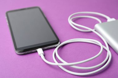 Mor arka planda akıllı telefon ve taşınabilir şarj aleti. Modern teknoloji