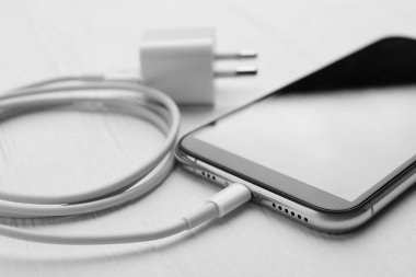 Akıllı telefon ve USB şarj aleti beyaz ahşap masada, yakın plan. Modern teknoloji