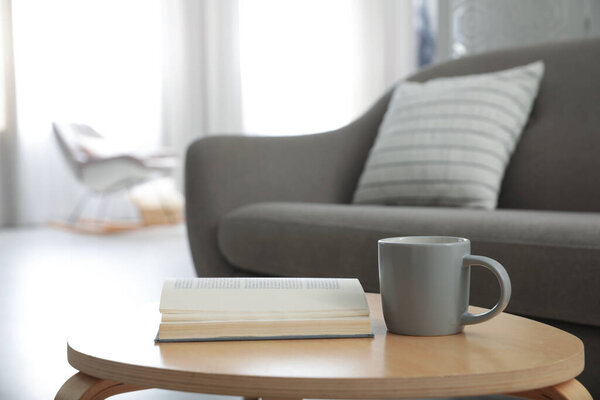 Book and cup of coffee on table near sofa. Interior design