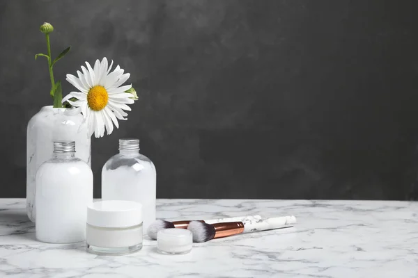 Composition with chamomile flower and cosmetic products on white marble table, space for text