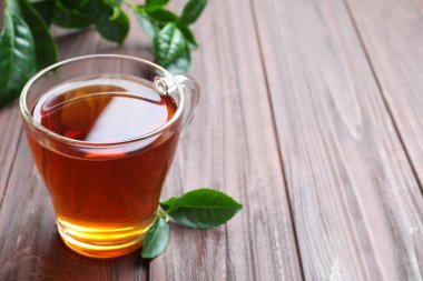 Cam bardak aromalı siyah çay ve ahşap masada yeşil yapraklar, metin için yer.