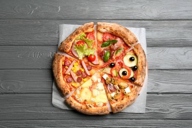 Gri ahşap masadaki farklı lezzetli pizzaların dilimleri.