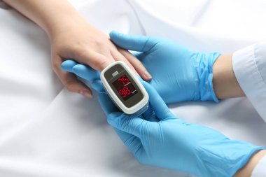 Doctor examining patient with fingertip pulse oximeter in bed, closeup clipart