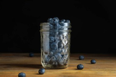 Tahta masada cam kavanozda olgun yaban mersinleri.