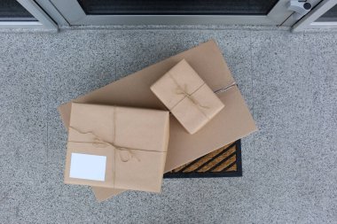 Giriş kapısının yanındaki paspasın üzerinde paketler var.