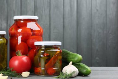 Gri ahşap arka planda farklı turşulu sebzelerle dolu cam kavanozlar. Metin için boşluk