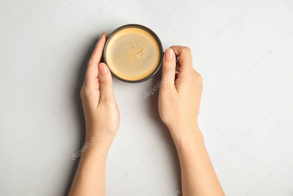 Woman with cup of coffee on light background, top view