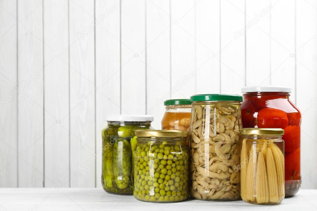 Glass jars with different pickled vegetables and mushrooms on white wooden background