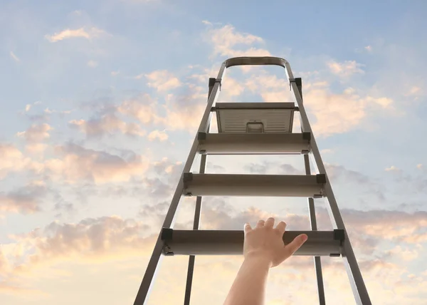 Woman climbing up stepladder against sky with clouds, closeup