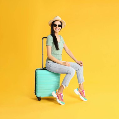 Sarı arka planda yaz gezisi için bavullu güzel bir kadın. Tatil gezisi