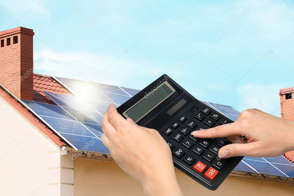 Woman using calculator against house with installed solar panels. Renewable energy and money saving