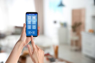 Akıllı evleri kontrol etmek için telefon uygulaması kullanan bir kadın.