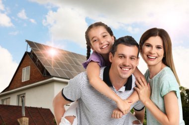 Evlerinin yakınında güneş panelleri olan mutlu bir aile. Alternatif enerji kaynağı