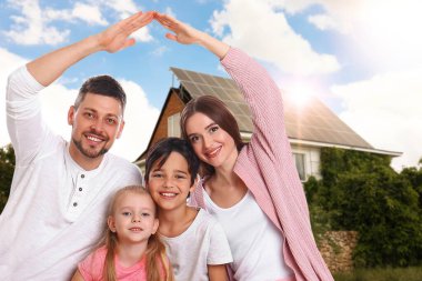 Evlerinin yakınında güneş panelleri olan mutlu bir aile. Alternatif enerji kaynağı