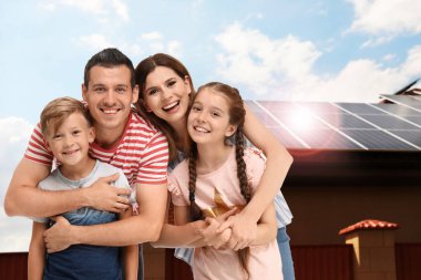 Evlerinin yakınında güneş panelleri olan mutlu bir aile. Alternatif enerji kaynağı