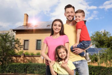 Evlerinin yakınında güneş panelleri olan mutlu bir aile. Alternatif enerji kaynağı